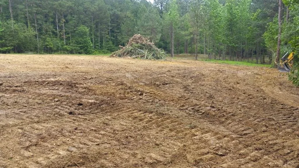 A cleared and graded lot with the brush pile stacked at the tree line